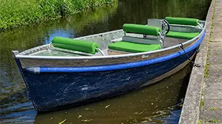 A boat for 2 people that you can rent in Giethoorn at Giethoorn Boat Rentals and has soft, green cushions and a steering wheel.